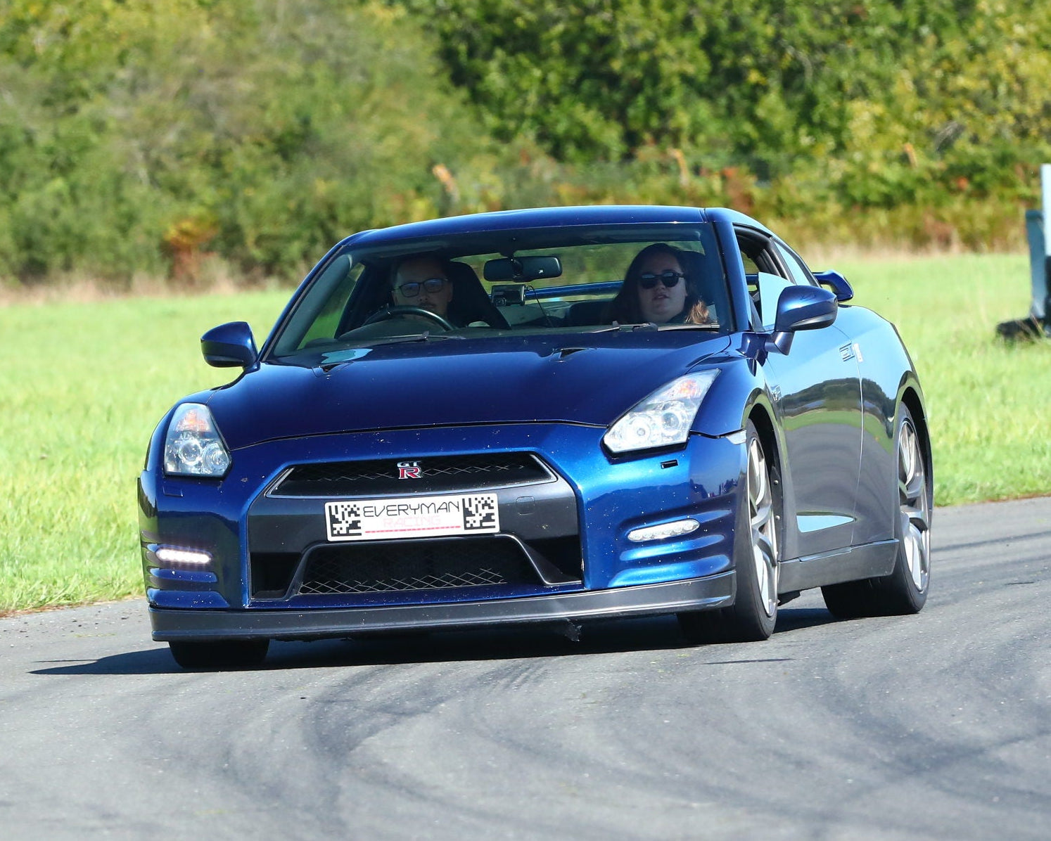 Blue sports car driving on a track with cones and greenery in the background