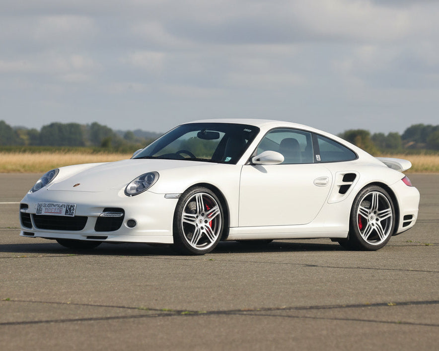 White Porsche sports car on a tarmac road with a clear sky background