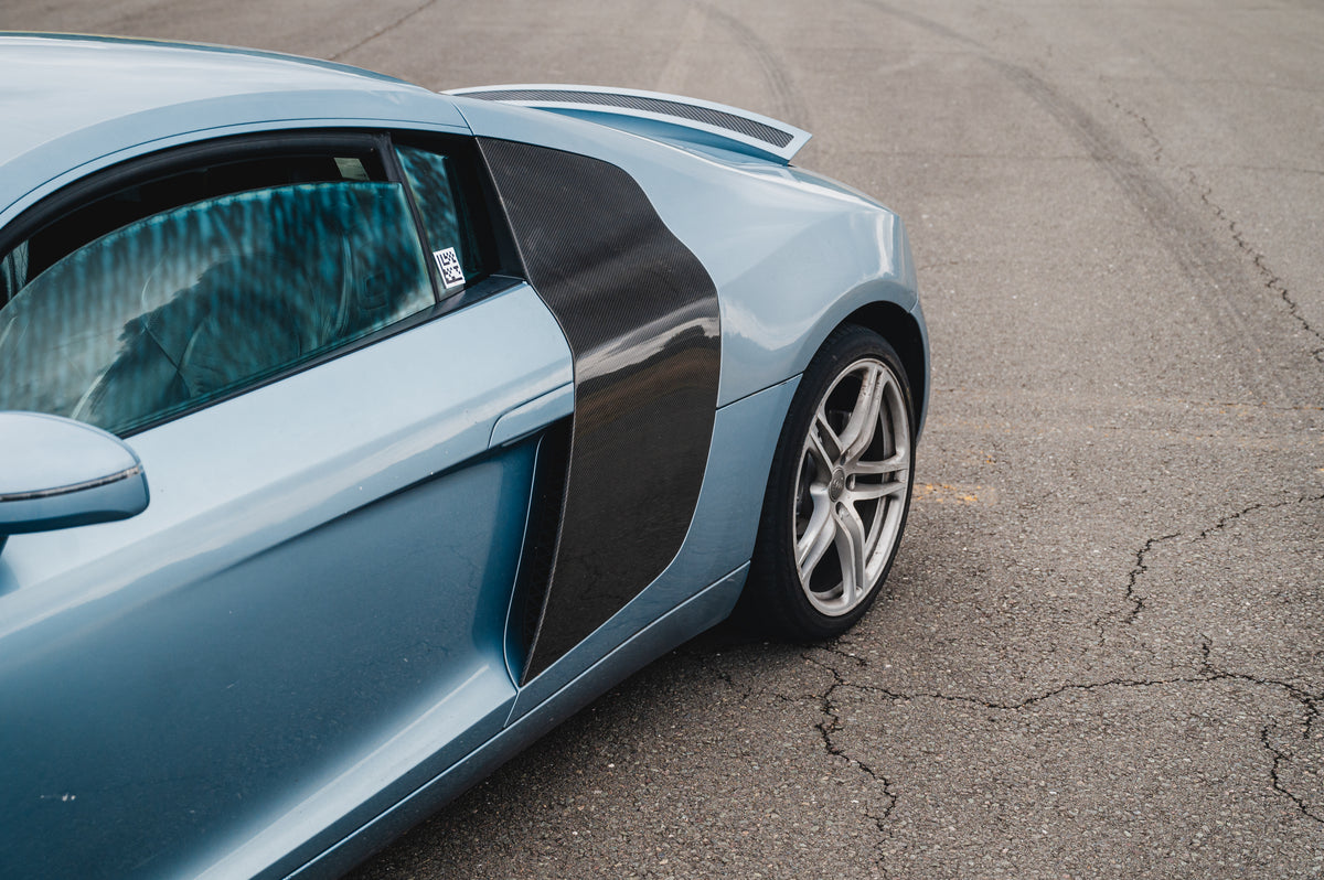 A light blue sports car with a prominent black side stripe, shown from a high-angle side view on an asphalt surface.