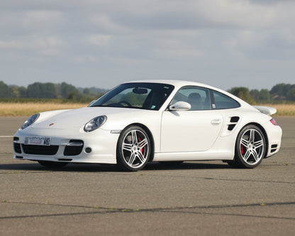 White Porsche sports car on a tarmac road with a clear sky background