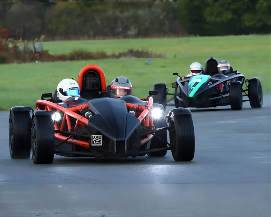Two racing ariel atom cars on a track with drivers wearing helmets.